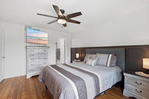 Primary bedroom with beautiful hickory flooring, decorative wood paneled wall, updated lighting with ceiling fan.