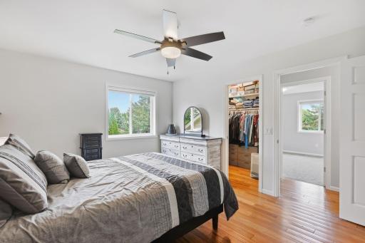 Primary bedroom with beautiful hickory flooring, decorative wood paneled wall, updated lighting with ceiling fan. Large walk in closet.