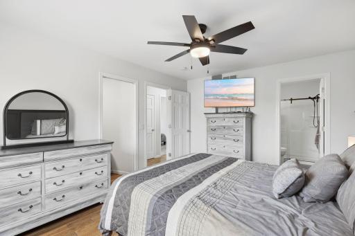 Primary bedroom with beautiful hickory flooring, decorative wood paneled wall, updated lighting with ceiling fan.