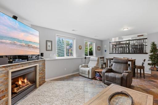 Pano of lower level family room with custom tile flooring, amazing stone gas fireplace surround, included 75" flat screen TV, light & bright sun filled room.