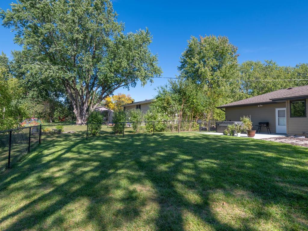 The fenced backyard offers a large lawn and mature trees.