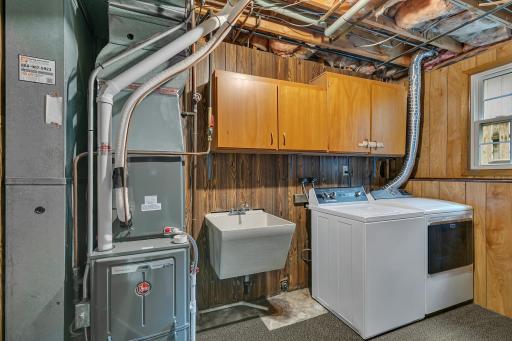 The laundry area includes a utility sink and cabinetry above the washer and dryer, both of which will remain with the home.