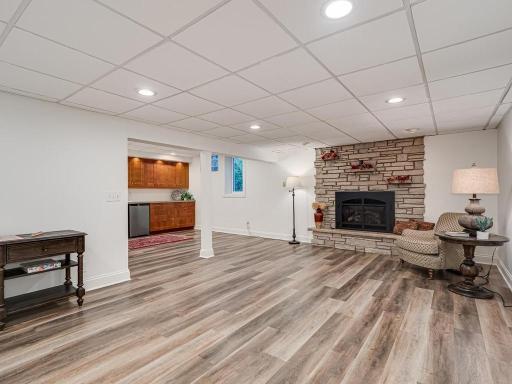 Lower Level family room or Mother in Law Suite features newer (2022) LTV vinyl plank floor , gas fireplace and kitchenette/wet bar with mini-fridge and custom cabinets.