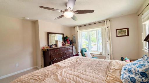 Serene primary bedroom with ceiling fan and warm natural light streaming through the windows.