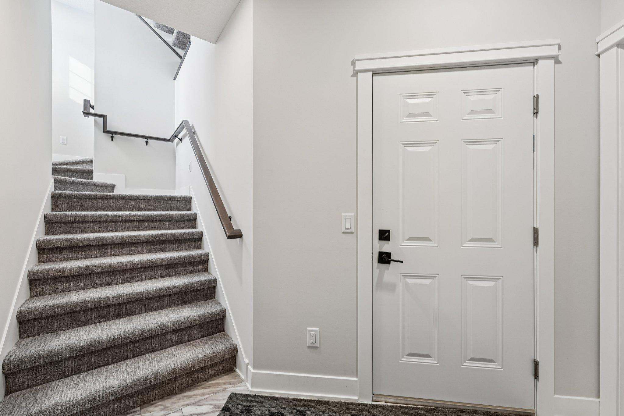 Lower-level stairway with plush carpeting and modern railing, providing easy access to the garage and additional spaces.