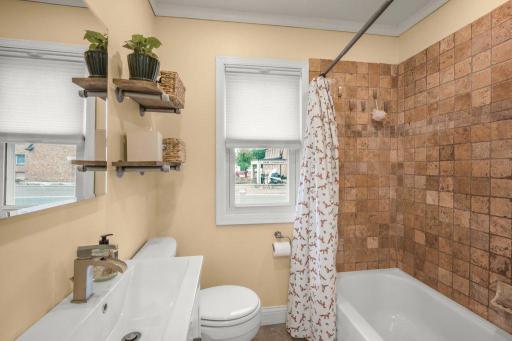 The main-floor full bath offers a clean, functional layout with a tiled tub surround, modern vanity, and natural light .