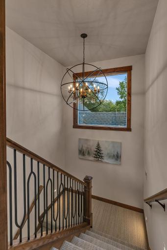 Elegant staircase features decorative wrought iron balusters with a classic wood handrail in addition to modern chandelier that serves as a sophisticated transition to bonus rooms above the garage.
