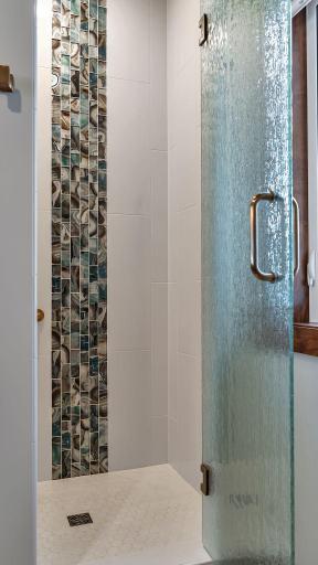 Primary bathroom custom tile design with glass shower door that swings out and in.