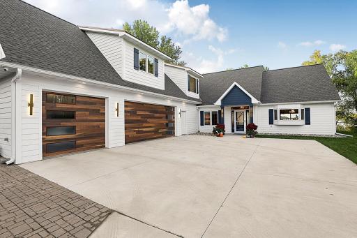 A striking facade featuring classic white horizontal siding (cement siding) contrasted by clean, dark shingle roof lines and custom peak architectural elements *Rich warm-toned natural wood plank garage door with vertical window accents.