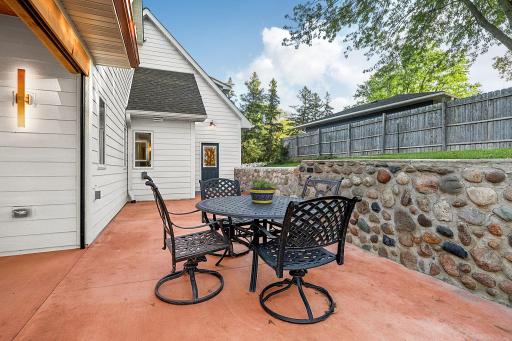 More patio with open layout transitions seamlessly into a lush green yard framed by privacy fence in addition to the stone retaining wall (stone came from the lake Latoka).
