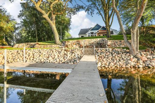 The meticulously landscaped shoreline boasts a stunning, tiered natural lake stone retaining wall, creating a dramatic and secure multi-level approach to the lakefront property.