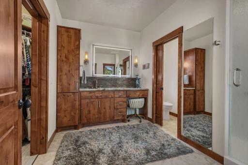 Rich, warm custom wood cabinetry provides ample storage with elegant warmth, perfectly contrasting with the contemporary backlit floating mirror. Enjoy the convenience of a built-in dedicated makeup vanity, premium stone countertop.