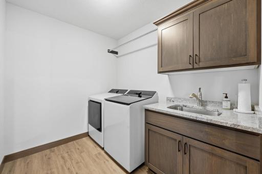 Spacious laundry room with granite top, undermount sink, upper/lower cabinets for extra storage, and hanging bar
