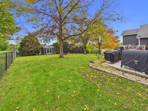 Fenced backyard with mature trees and a landscaped area beside the home