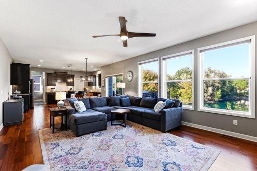 Hardwood floors anchor the open-concept main level, creating a clear flow between the living room, dining area, and kitchen. Large windows stretch across the back of the home, drawing in natural light and framing a quiet, uninterrupted view of the ne