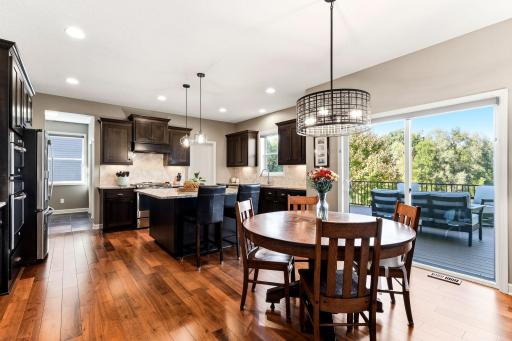 The kitchen features dark cabinetry, a granite center island, and an adjacent dining area that opens directly to the outdoor composite deck.