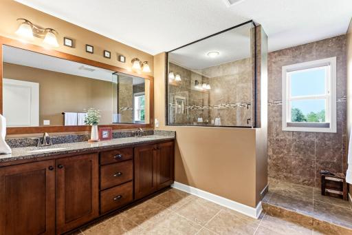 Step into the luxurious en-suite primary bathroom, showcasing a premium dual vanity with stone countertops and an oversized glass-enclosed shower