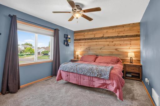 Spacious upper-level primary suite featuring a beautiful wood accent wall, ceiling fan, and plenty of natural light.