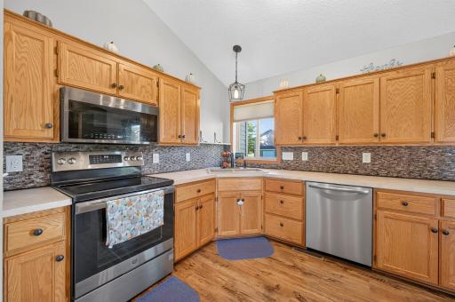 Bright, open kitchen featuring vaulted ceilings, abundant cabinetry, stainless-steel appliances, and plenty of counter space.