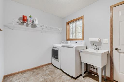 Convenient laundry room located on main floor featuring a washer and dryer, utility sink, and additional shelving for storage. A window provides natural light to this functional household space.