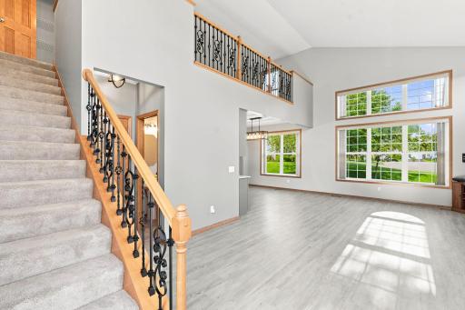 Dramatic two-story living room with oversized windows, updated flooring, and a gas fireplace.