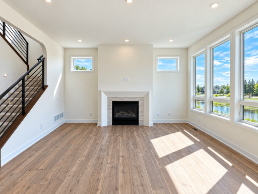 Sun-filled great room featuring expansive windows, warm wood flooring, a modern fireplace, and contemporary open-railing staircase.