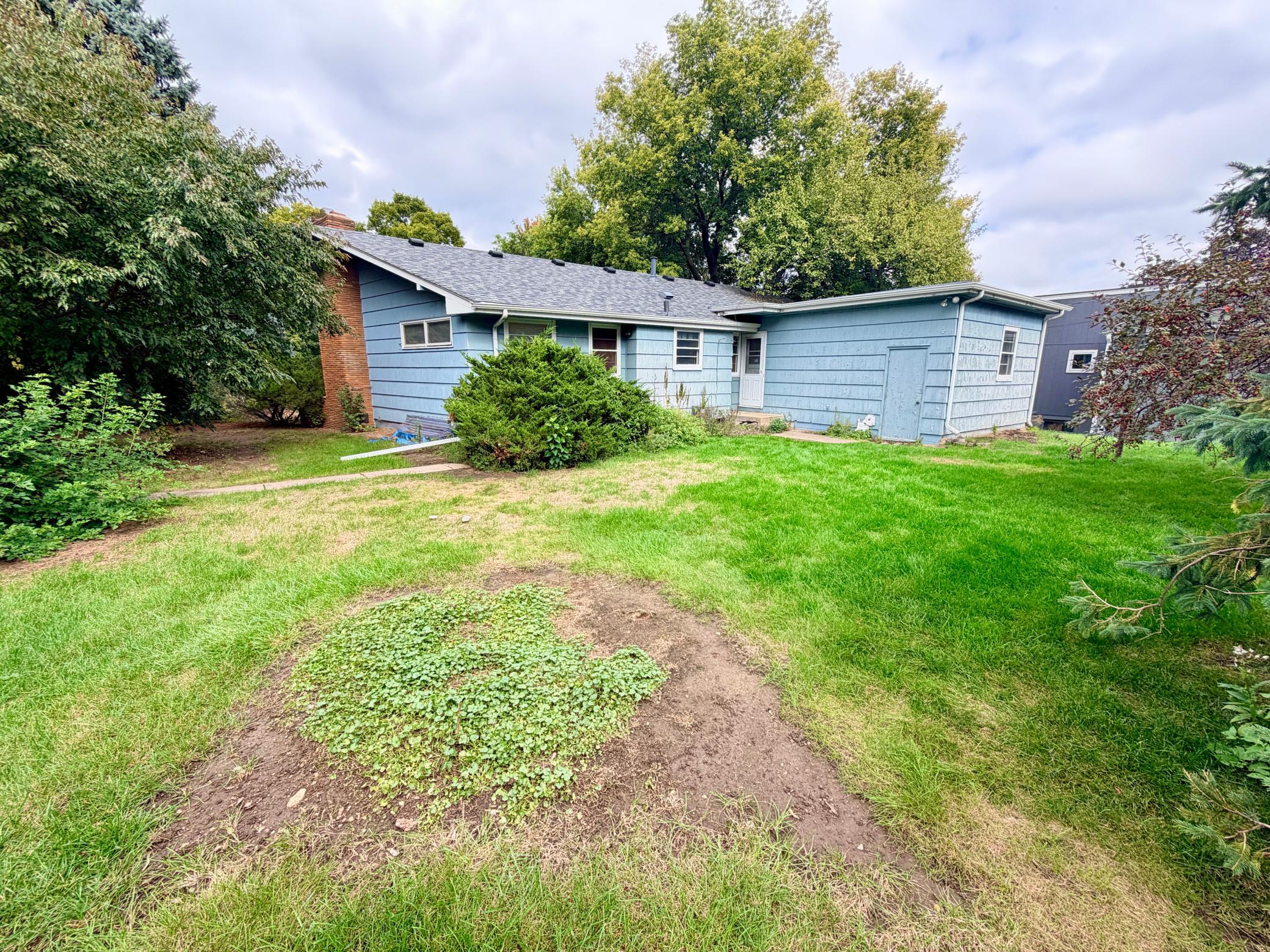 The large, flat back yard of this corner lot has mature perimeter landscaping for privacy. The back door is near the kitchen for easy access. The blue door on the addition provides access to an attached storage shed.