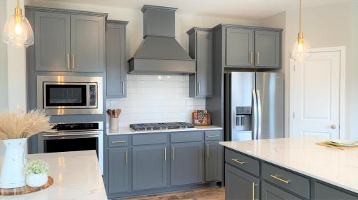 This home features our gourmet kitchen with wood hood, 36" gas cooktop, built-in wall oven & convection microwave and more! Photo of model home, colors and finishes vary.