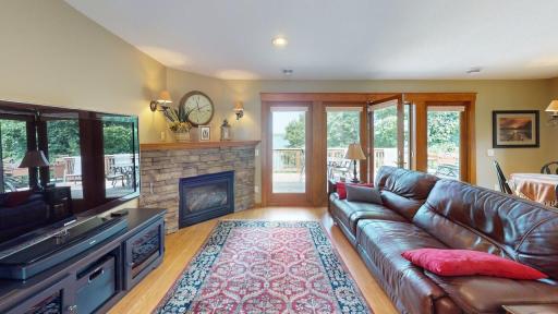 Warm and inviting living room featuring a stone gas fireplace, hardwood floors and glass doors that open to the spacious lakeside deck.