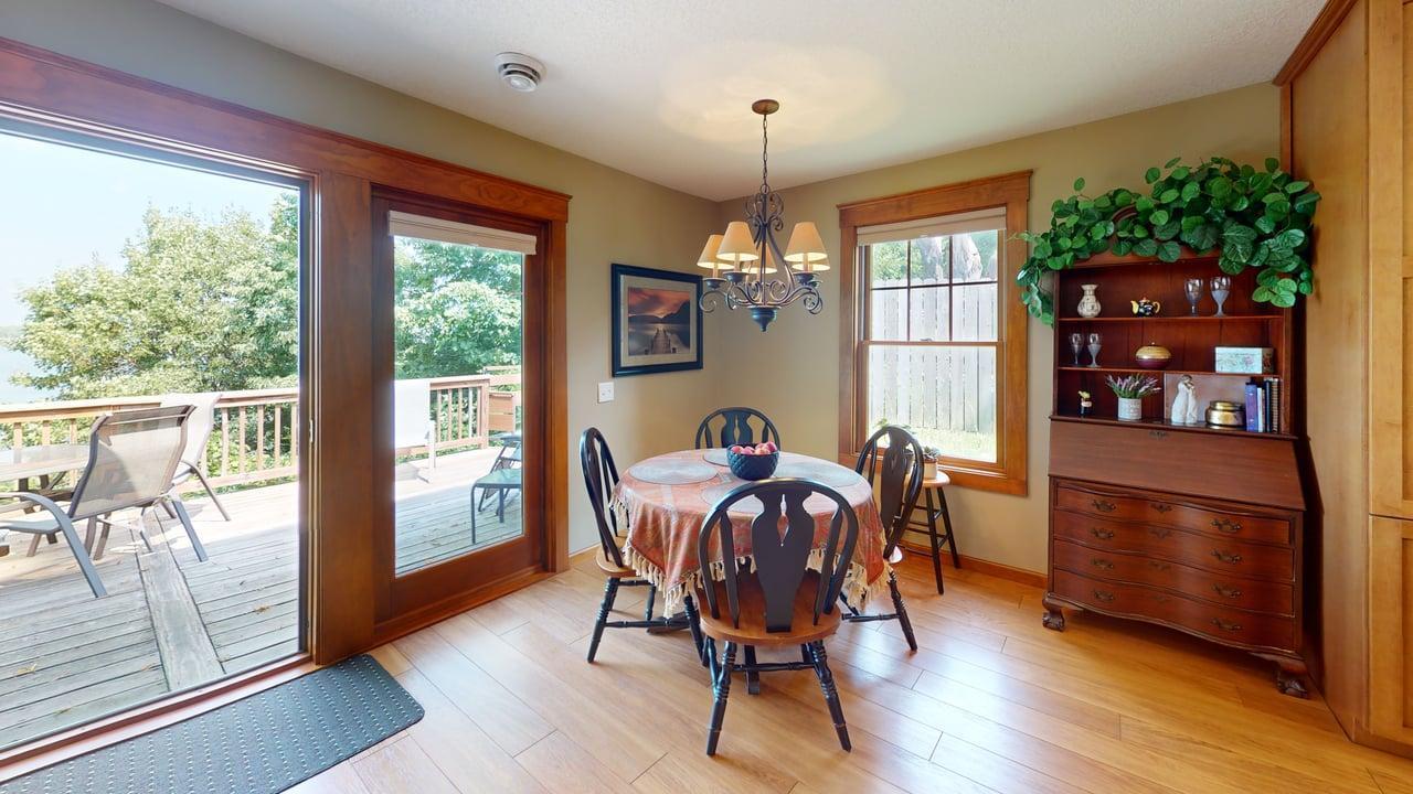 Informal dining room surrounded by windows with glass doors opening to the lakeside deck, creating an easy flow for indoor-outdoor dining.