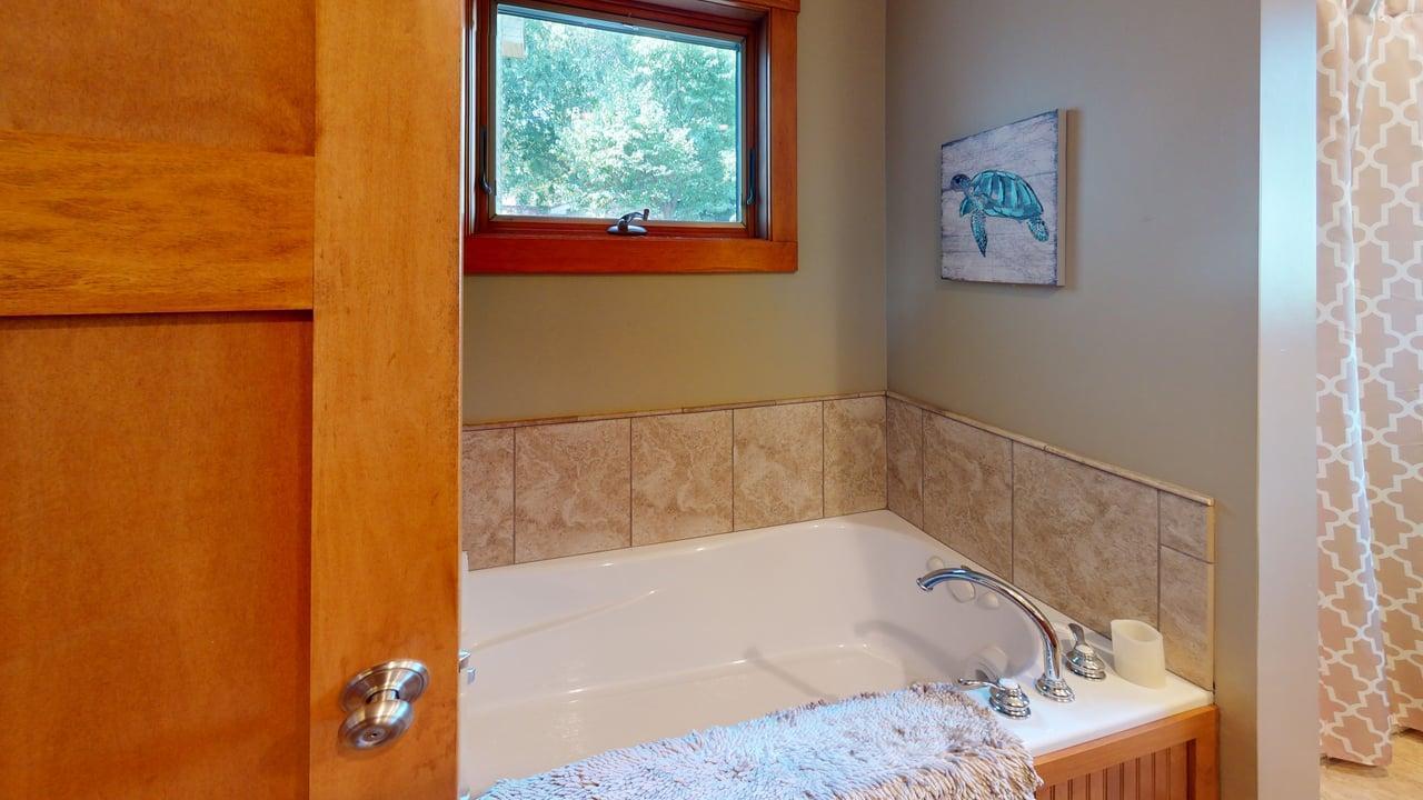 Main-level full bathroom features a relaxing jetted tub surrounded by tile and a window bringing in fantastic natural light.
