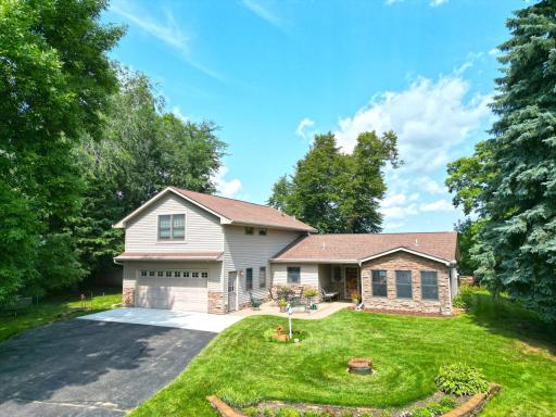 Beautifully maintained year-round home surrounded by mature trees and landscaping, offering a welcoming patio area.