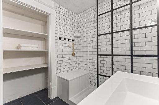 The bathroom offers tile flooring, a walk-in rain shower, built-in shelving and a vanity with additional storage.