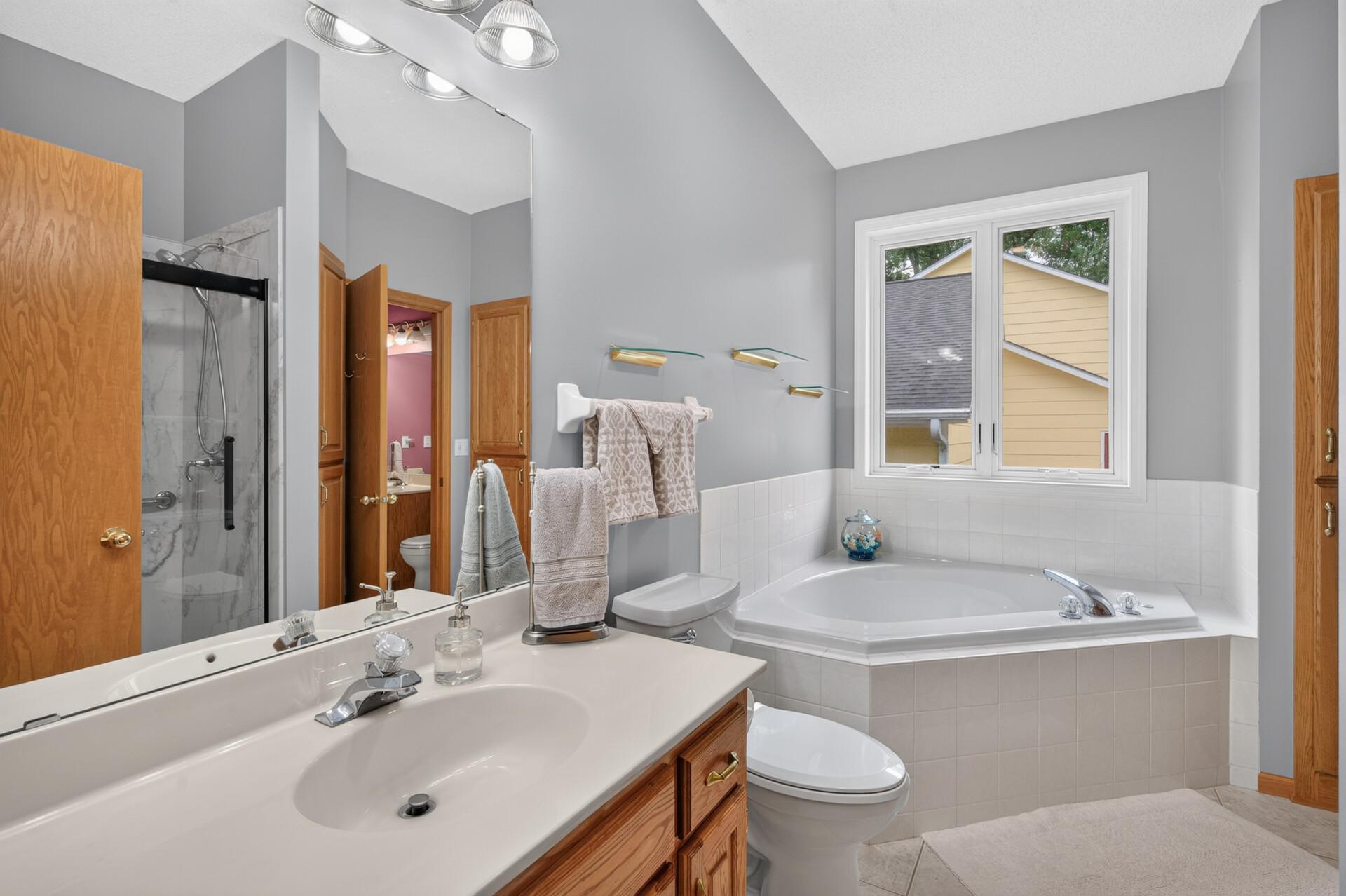 The main floor bathroom offers a corner whirlpool tub with window above it, linen closet ceramic tiled floor and newer shower.