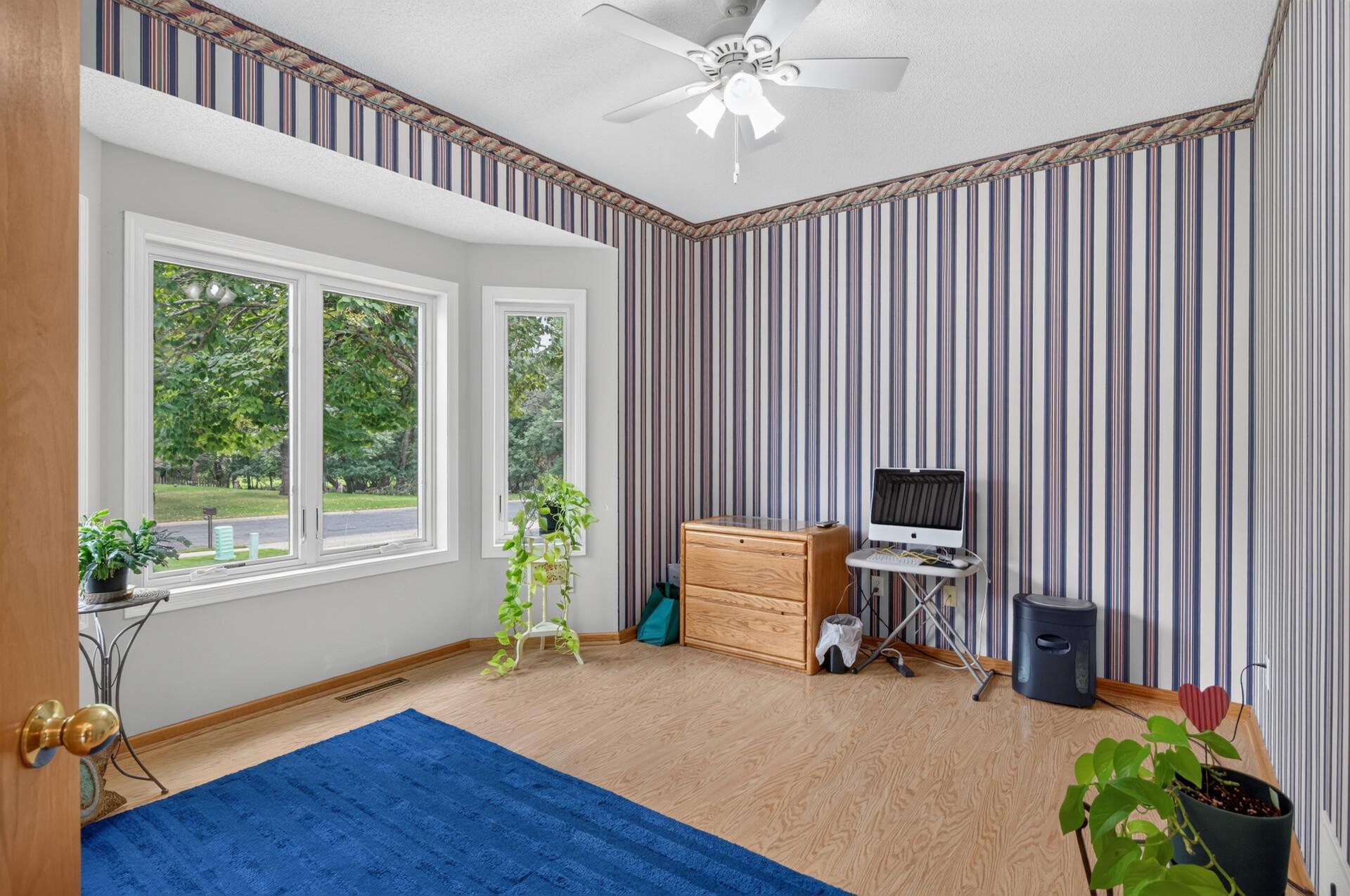 Large bayed window in the front bedroom/office with a ceiling fan.