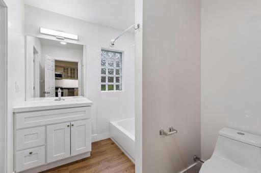 Unit 1: The main-floor full bath features updated flooring, a vanity sink, overhead lighting, and a tub/shower combo for a clean and functional space.