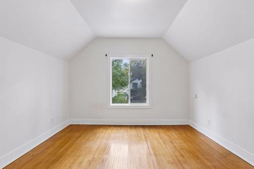 Unit 2: Natural light fills this first of 2 upper-level bedrooms through a bright window, complemented by hardwood flooring and overhead lighting.