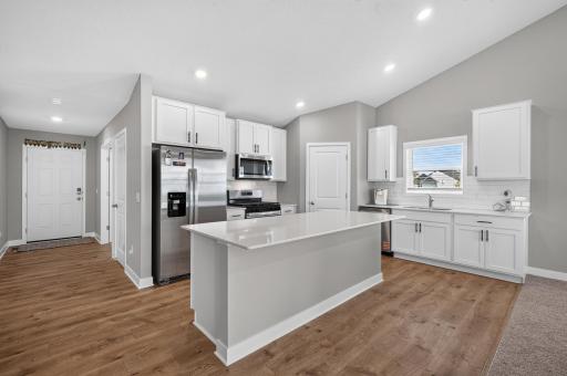 The beautiful kitchen features crisp white cabinetry, quartz countertops, stainless steel appliances, and a stylish ceramic tile backsplash. A spacious center island provides plenty of room for meal preparation, casual dining.