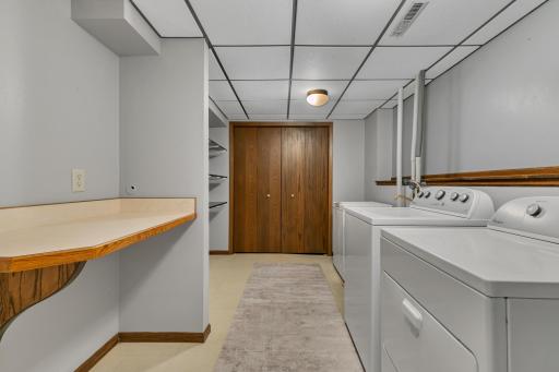 The spacious laundry room provides excellent functionality with a folding table, adjustable built-in shelving, utility sink, and Whirlpool washer and dryer that will remain. A chest freezer next to the utility sink may also stay.