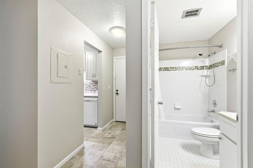 Updated full bath features a tiled tub/shower surround with decorative accent, handheld shower and crisp neutral finishes