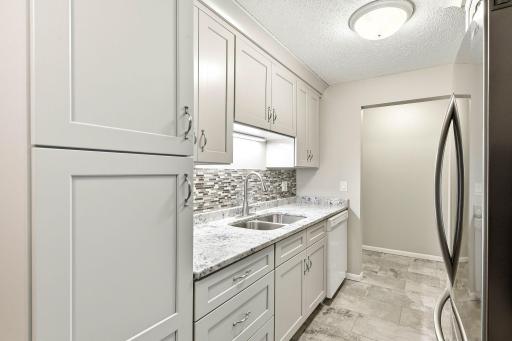 Beautifully updated kitchen featuring granite countertops, tile backsplash, stainless steel refrigerator and abundant cabinetry for storage.