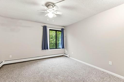Spacious bedroom with neutral finishes, ceiling fan and a large window overlooking mature trees.