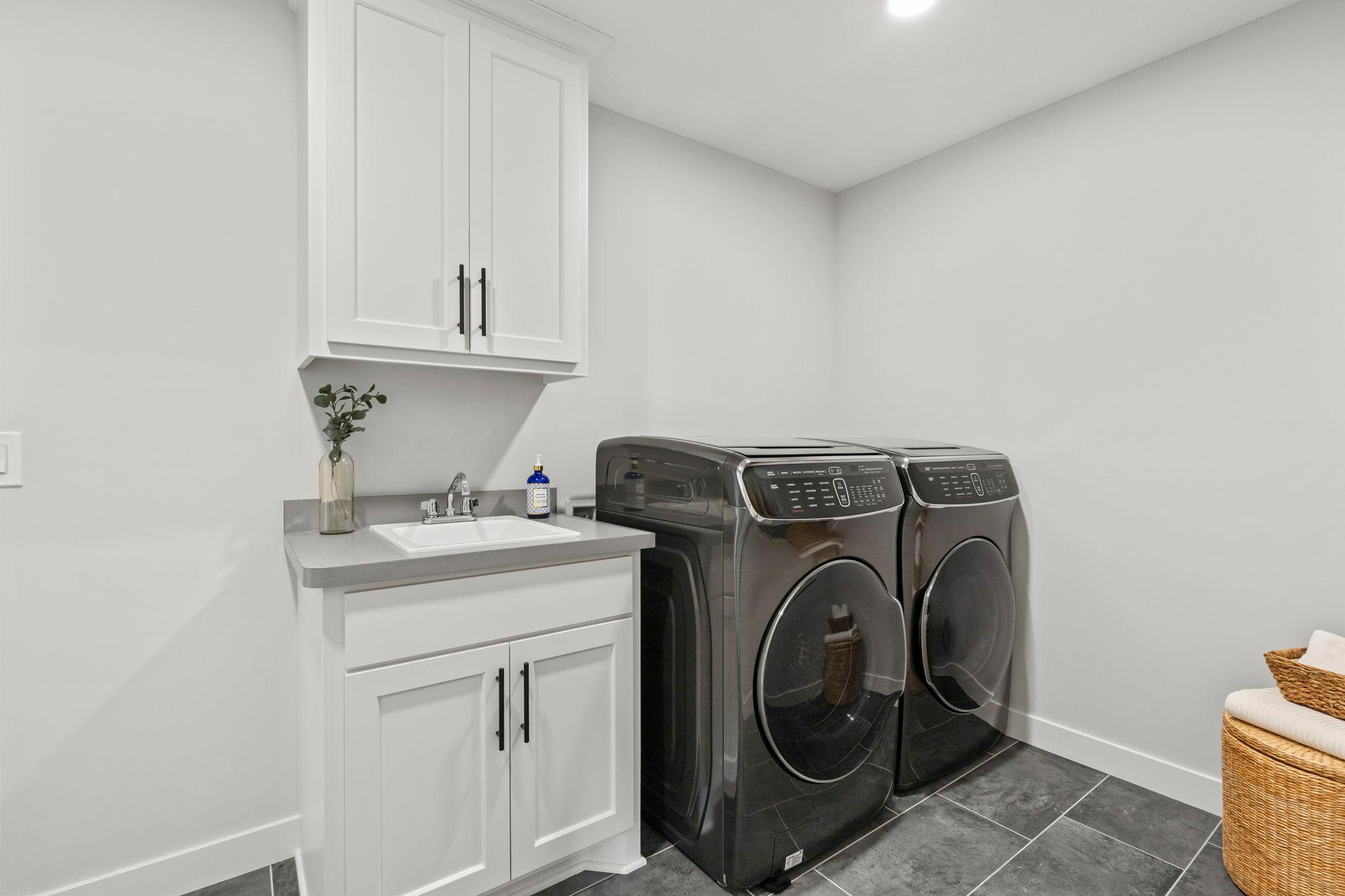 The upper-level laundry room, complete with a utility sink, cabinetry, tile flooring, and front-loading washer and dryer for ultimate convenience.