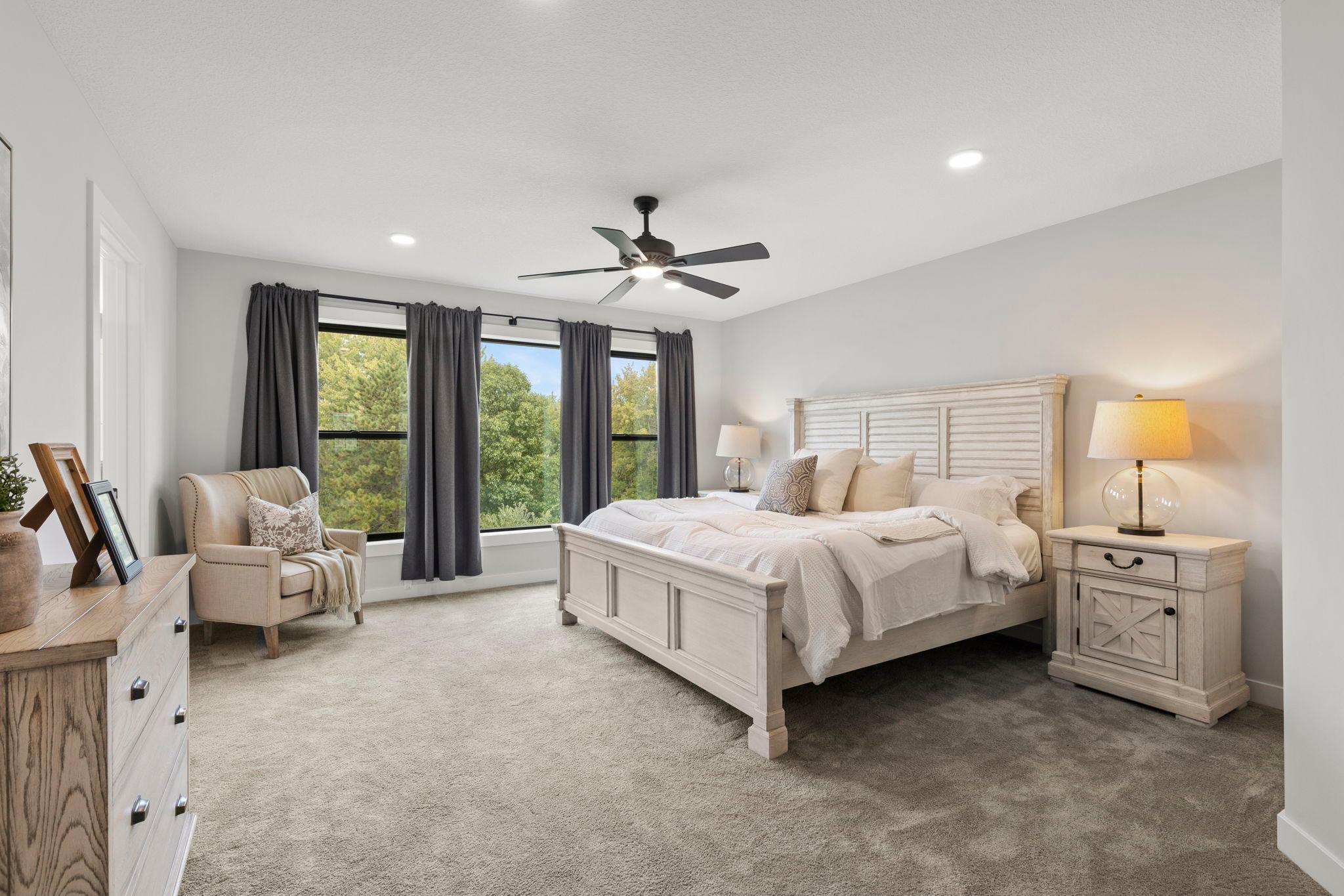 The upper level offers four bedrooms, including a spacious primary suite featuring plush carpeting, large rear-facing windows that fill the room with natural light, and a ceiling fan.