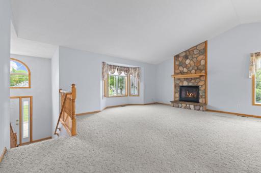 The living room is filled with natural daylight and showcases soaring vaulted ceilings that create a bright, open feel. A stunning floor-to-ceiling rock fireplace serves as the focal point of the room, adding warmth, a perfect setting for relaxing.
