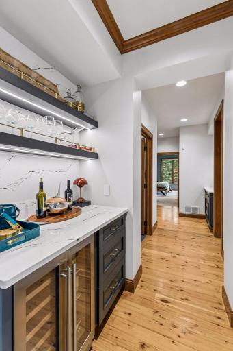 Stylish built-in bar with quartz counters and backsplash, illuminated floating shelves, brass accents, and a beverage fridge, conveniently tucked between the dining area and kitchen