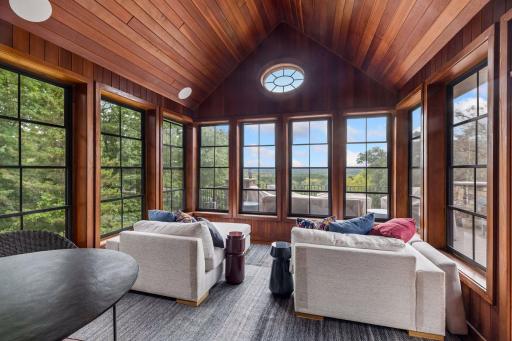 Walls of windows, warm wood tones, and a vaulted ceiling make this three-season porch a year-round favorite for soaking in the views