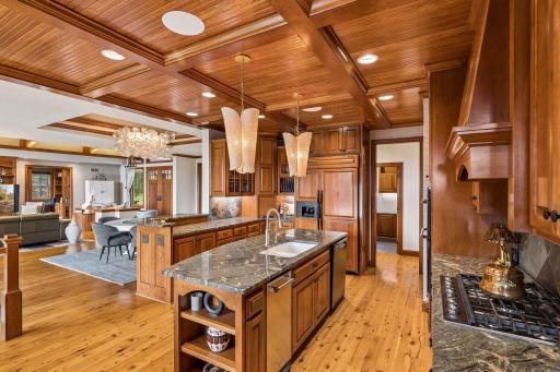 Gourmet kitchen with a coffered beadboard ceiling, custom cherry cabinetry, slate backsplash, and granite counters, opening to a cozy keeping room with a stone fireplace and porch access