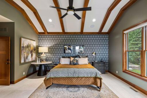 Vaulted beams and a dramatic wallpaper accent wall anchor this designer primary bedroom