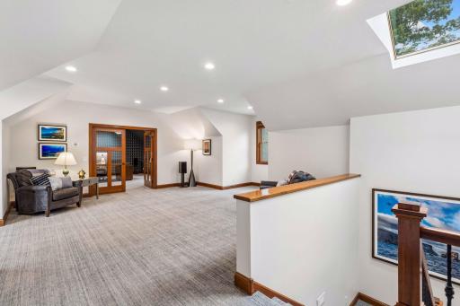 Expansive upper-level bonus room with vaulted dormer ceilings, a skylight, and recessed lighting, offering flexible space for a media room, game room, or lounge, with French doors opening to an adjacent 5th bedroom / office
